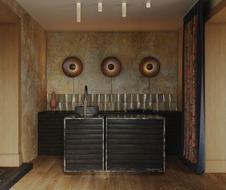 A dark-toned kitchen with tactile walls, and large architectural wall lights