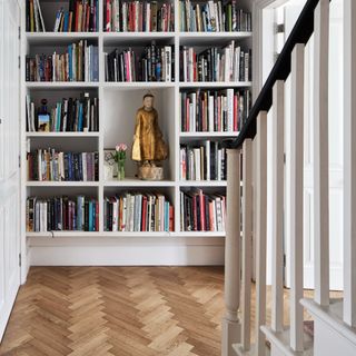 A hallway with a built-in library and light wood herringbone flooring