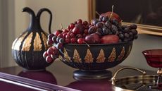 Black and gold pitcher and bowl filled with red fruit on a lacquered red surface
