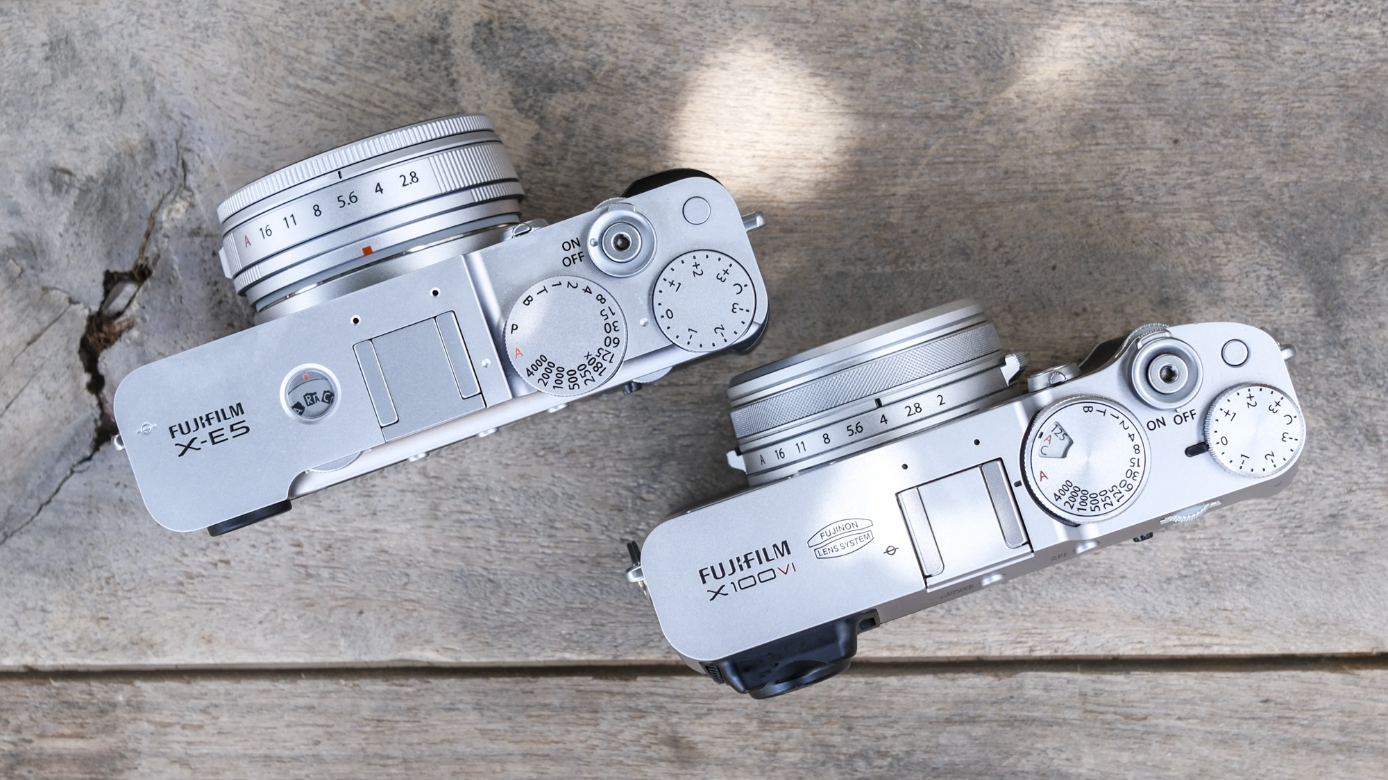 Top down view of the Fujifilm X-E5 alongside the Fujifilm X100VI, on a wooden bench