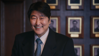 Veteran Korean actor Song Kung-ho plays Park Doo-chill (aka Uncle Samsik) in a dark business suit, smiling in a wood-lined office