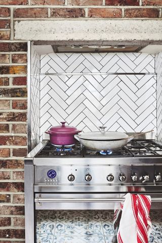 A kitchen stove with white herringbone tiles and exposed brick wall background
