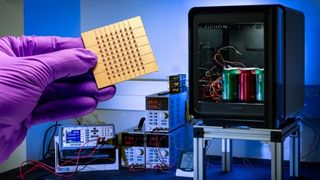 A Samsung and Johns Hopkins APL Peltier effect cooling device being held up by a hand with a lab glove, with various electronic gubbins going on in the background