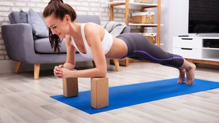 Woman performing a plank resting elbows on yoga block during home workout on exercise mat