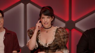 Emily Axford, playing a vampire, holds a finger up to an imaginary earpiece