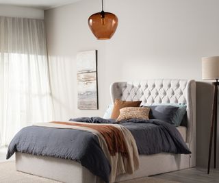 brown glass pendant light in bedroom above cream bed with blue and brown bedding