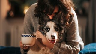 Woman holding a mug of tea and hugging her dog