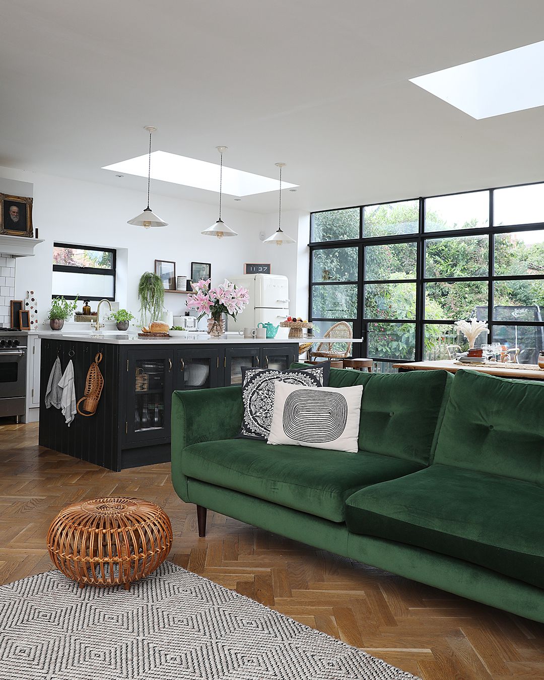 A kitchen extension with roof glazing and Crittal-style doors with a green velvet sofa and kitchen island