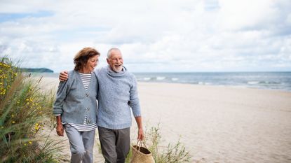 An older couple walks together on the beach.