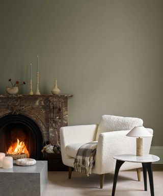 taupe sage green living room with open fireplace and white boucle armchair