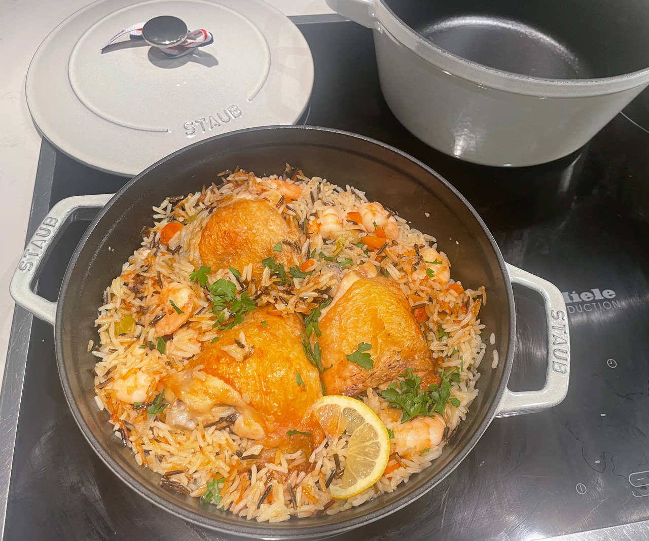 A two handled pan on an electric stove with chicken and rice inside. The pan lid sits on the stove behind it.