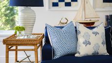 A living room with a dark blue couch, two throw pillows, and a rattan side table to the left with a lamp on top of it