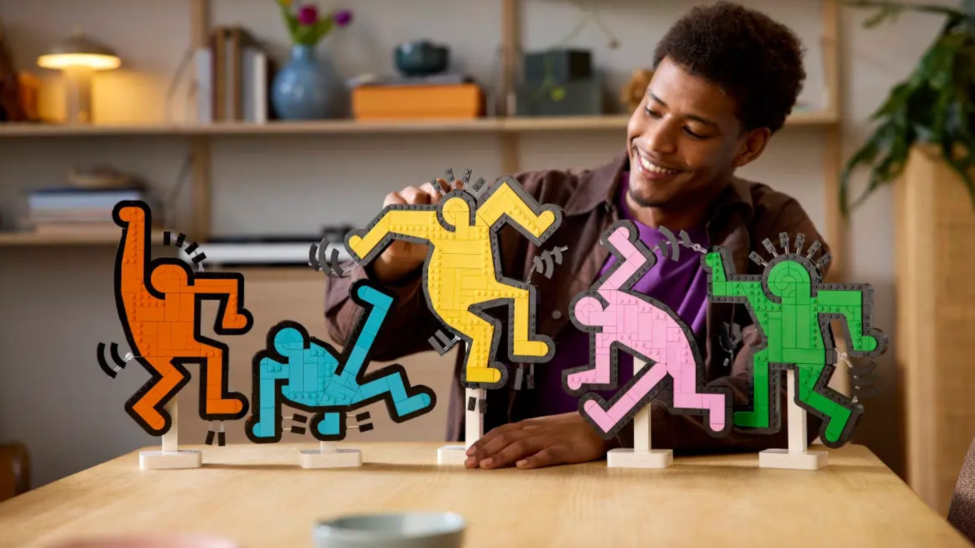 A smiling man handles the Keith Haring -Dancing Figures set as it stands on a table