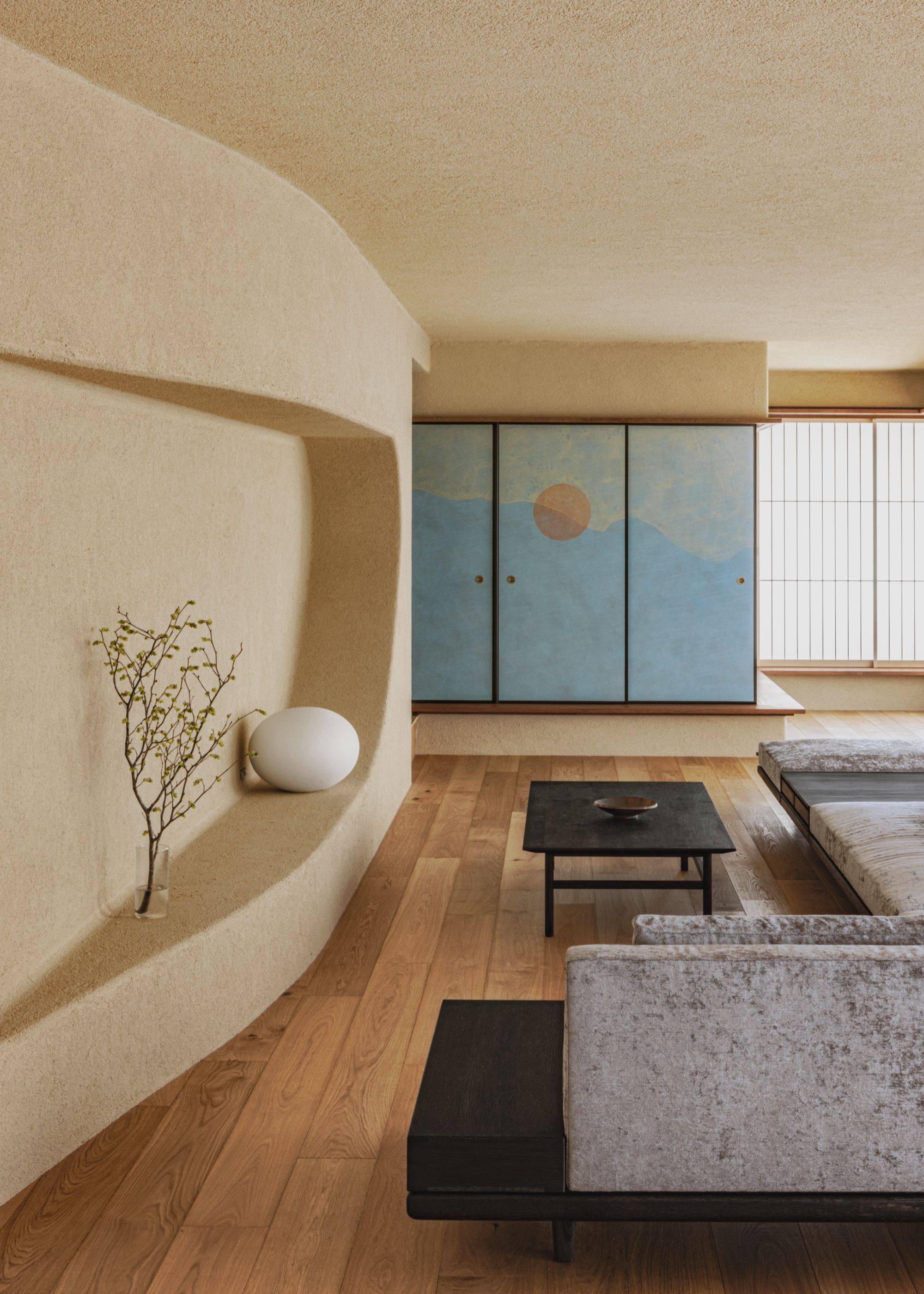 Sliding internal doors painted in blue at the bottom and gold at the top with an orange sun-like circle in the center are closed next to a minimalist Japanese living space with a low-profile sofa