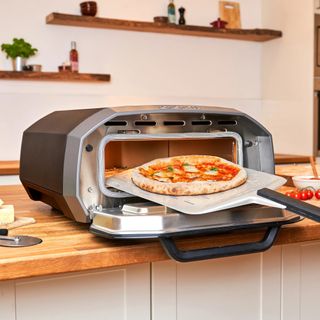 The Ooni Volt 12 (an indoor and outdoor pizza oven) in a kitchen, being used to cook a pizza