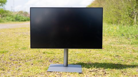 A black BenQ PD3225U monitor sitting on grass in sunshine