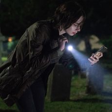 emma myers as pip shining a flashlight on a grave and looking at her phone in a good girl's guide to murder season 3