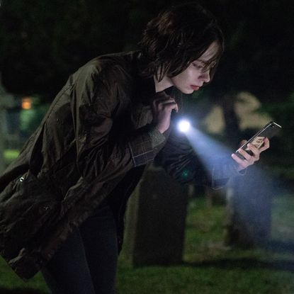 emma myers as pip shining a flashlight on a grave and looking at her phone in a good girl's guide to murder season 3