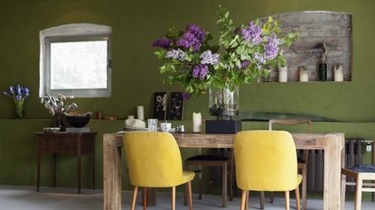 Stylish dining room with vase of long lilac stems on wooden table