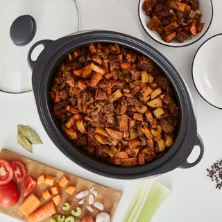 slow cooker with stew and chopping board of vegetables