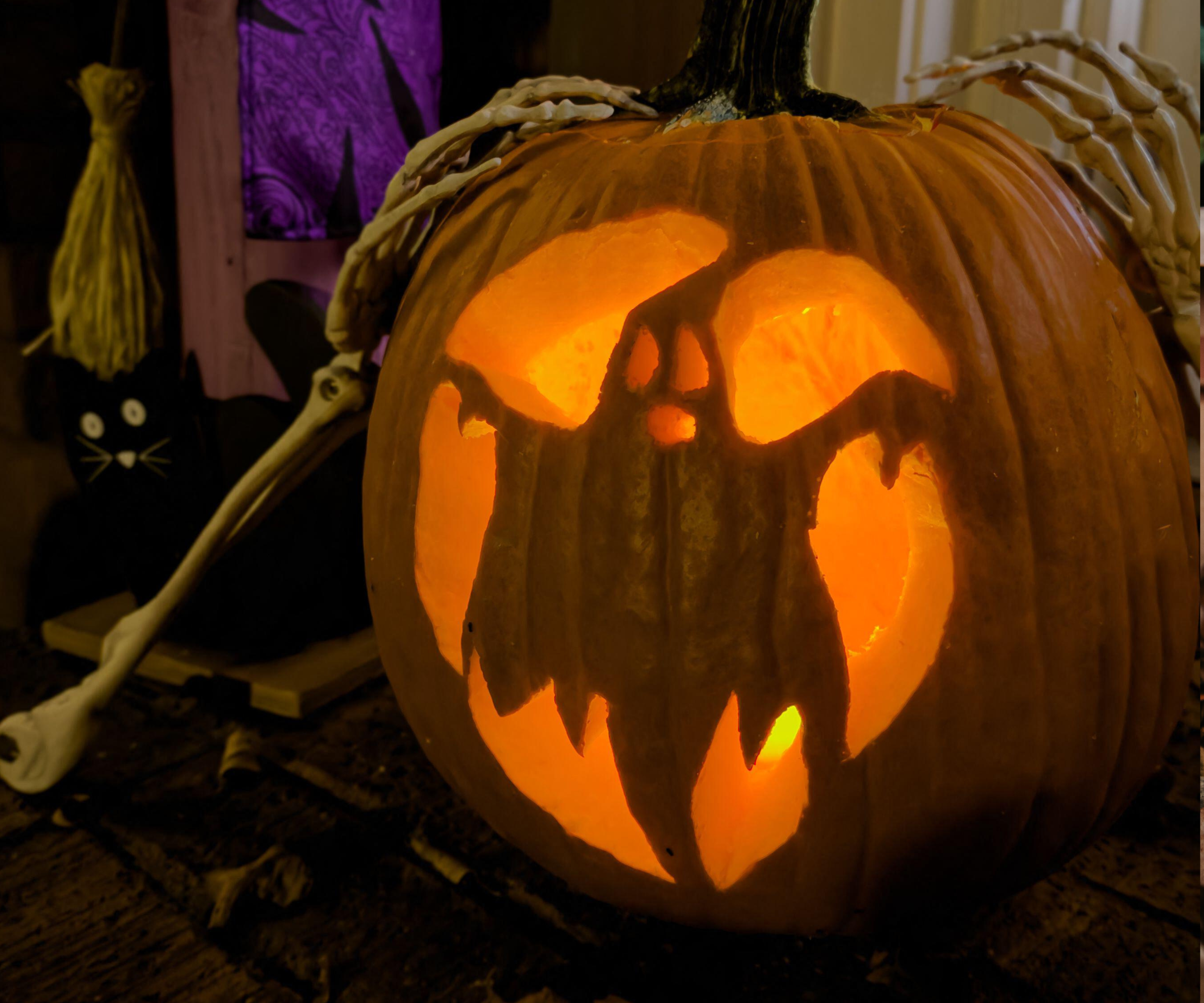 A pumpkin carved with an image of a ghost glows with an orange candle as part of a home's Halloween decorations.
