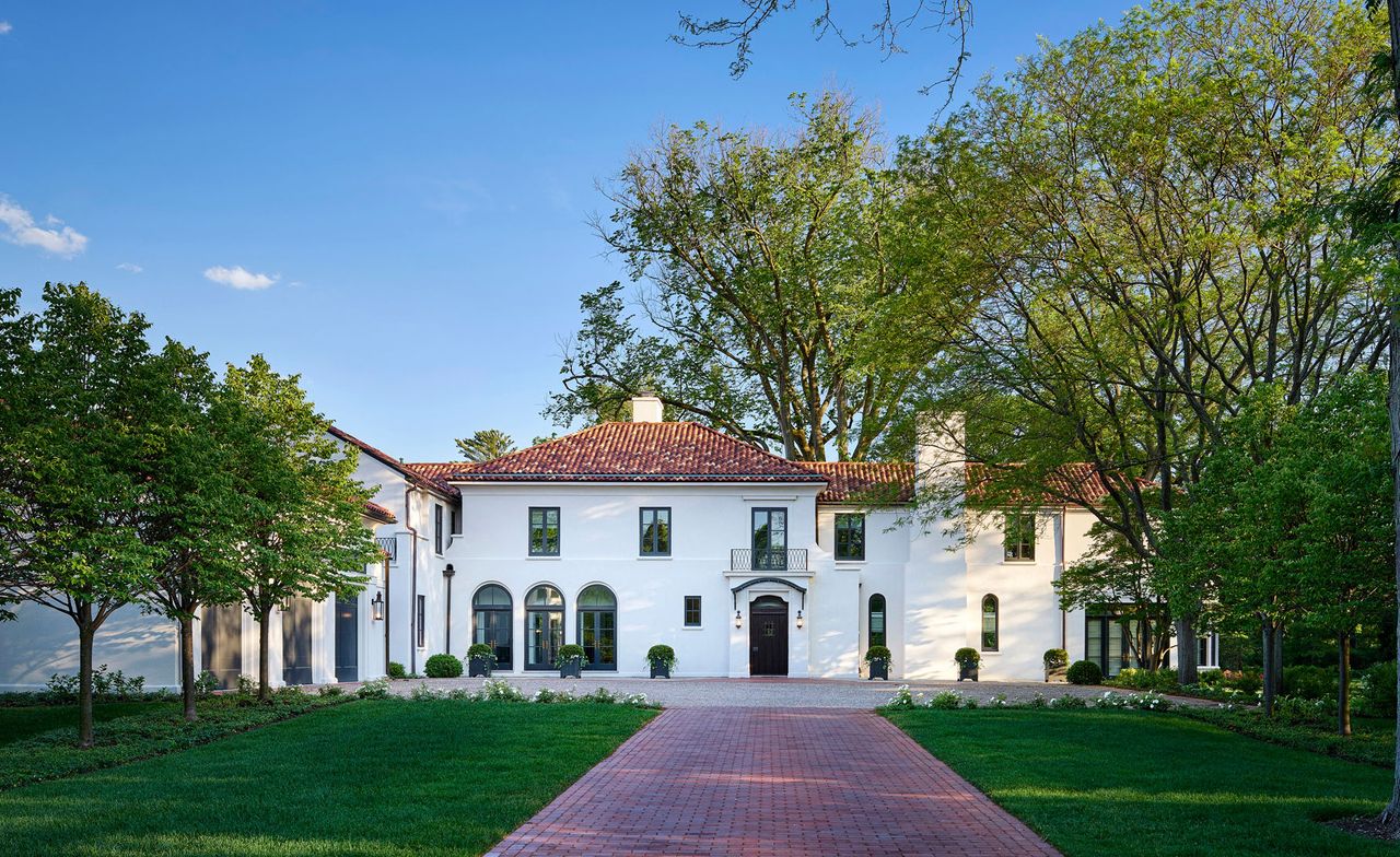 front facade and driveway to grand white home with trees and blue skies 