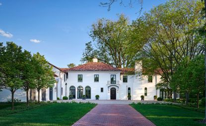 front facade and driveway to grand white home with trees and blue skies 