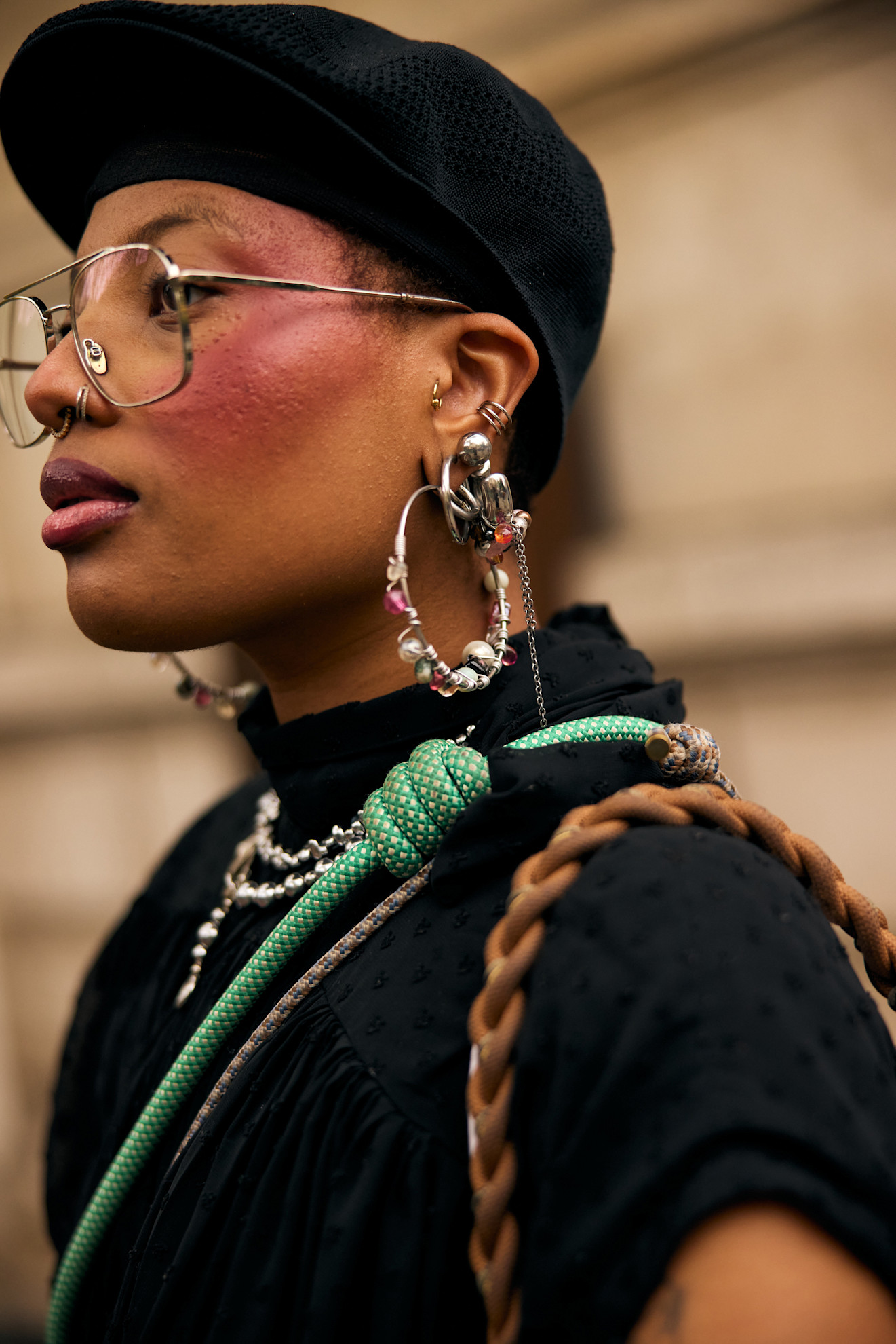 a black woman with silver earrings in a black shirt and hat wearing lots of blush