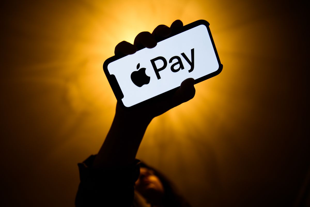 A person holding a smartphone with the Apple Pay logo displayed