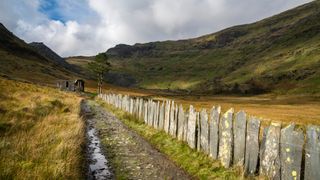 A slate-edged path leading towards a ruined cottage and mountains at Blaenau Ffestiniog, Wales