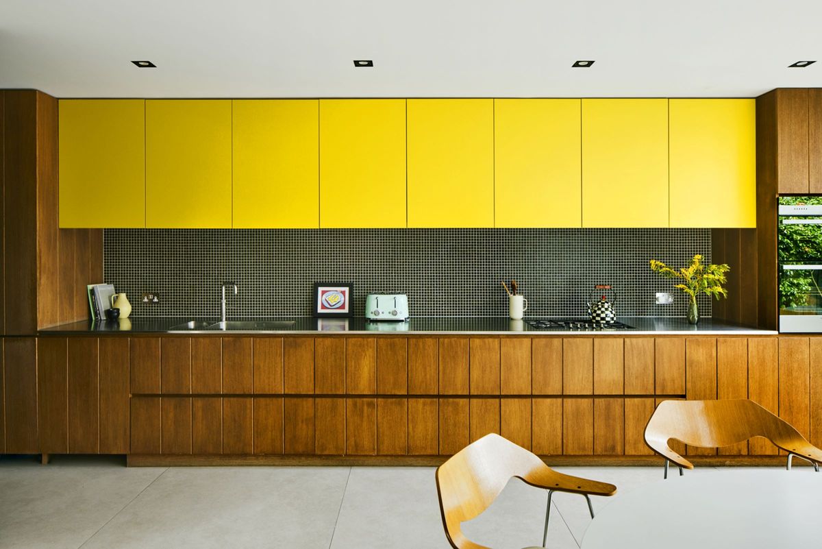 Brown kitchen cabinets and yellow overhead cabinets line the kitchen