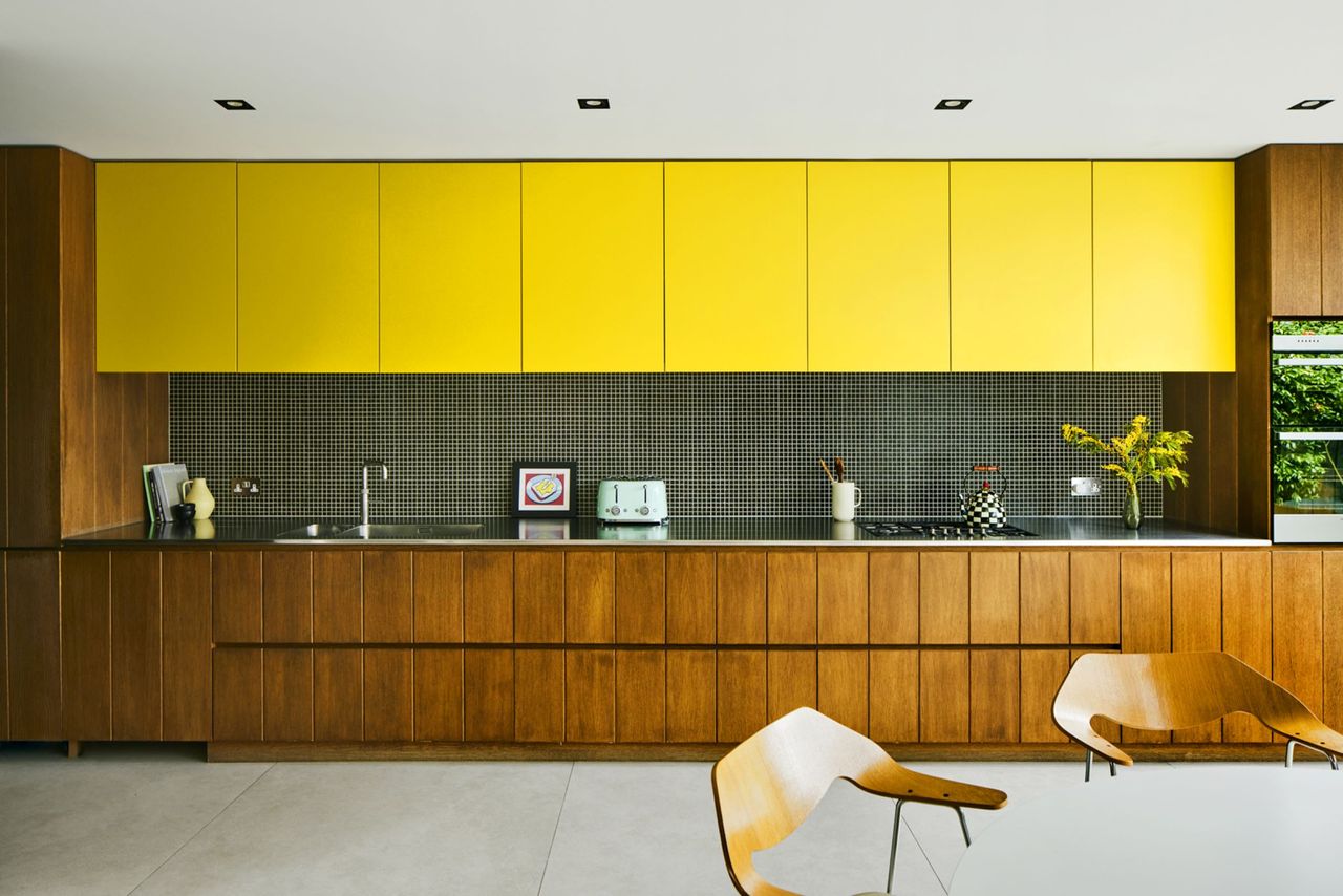 Brown kitchen cabinets and yellow overhead cabinets line the kitchen