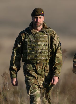 Prince William wearing army fatigues and a green beret walking through grass