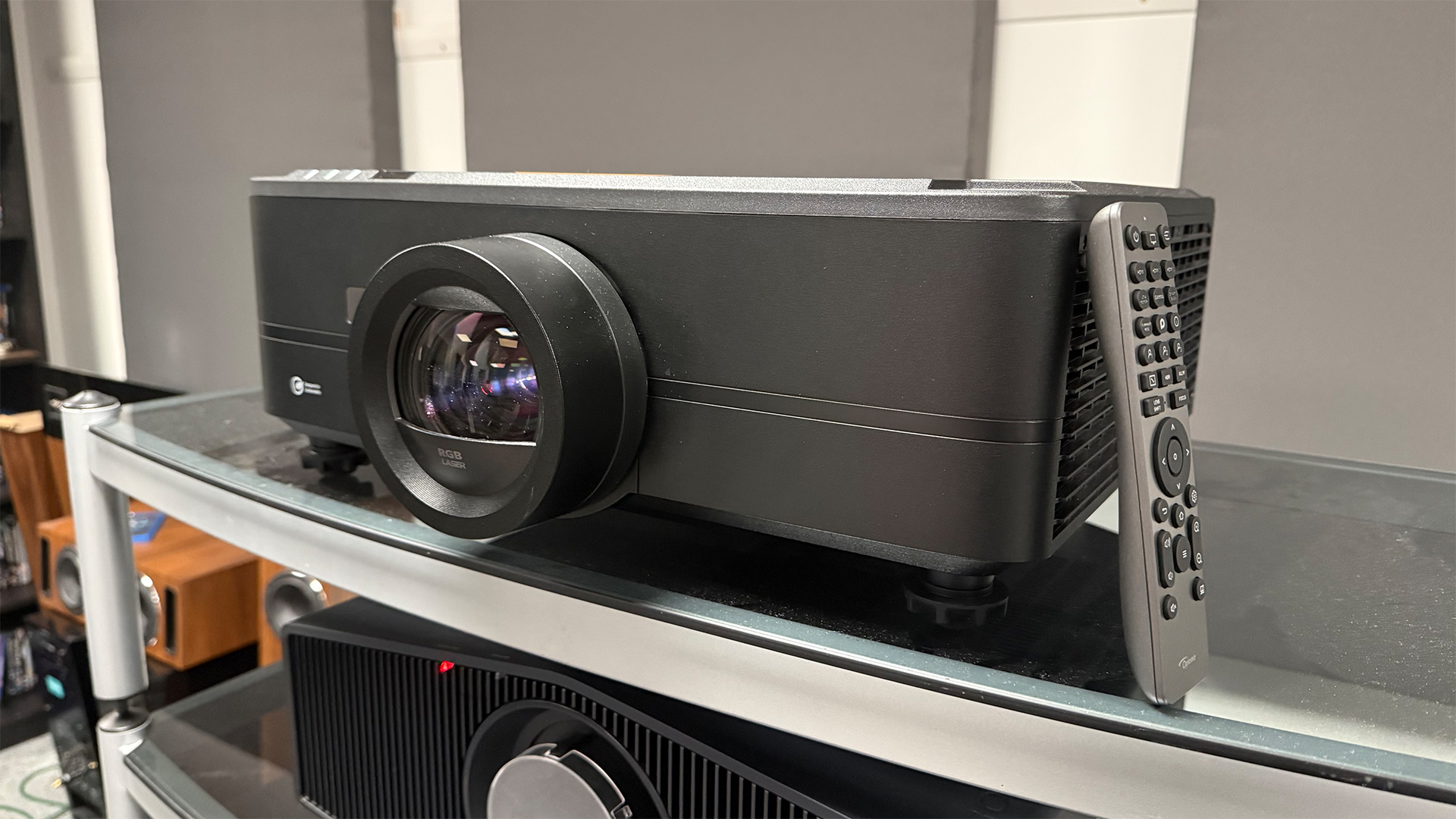 Optoma UHZ78LV home cinema projector on glass topped unit with remote leaning up against it
