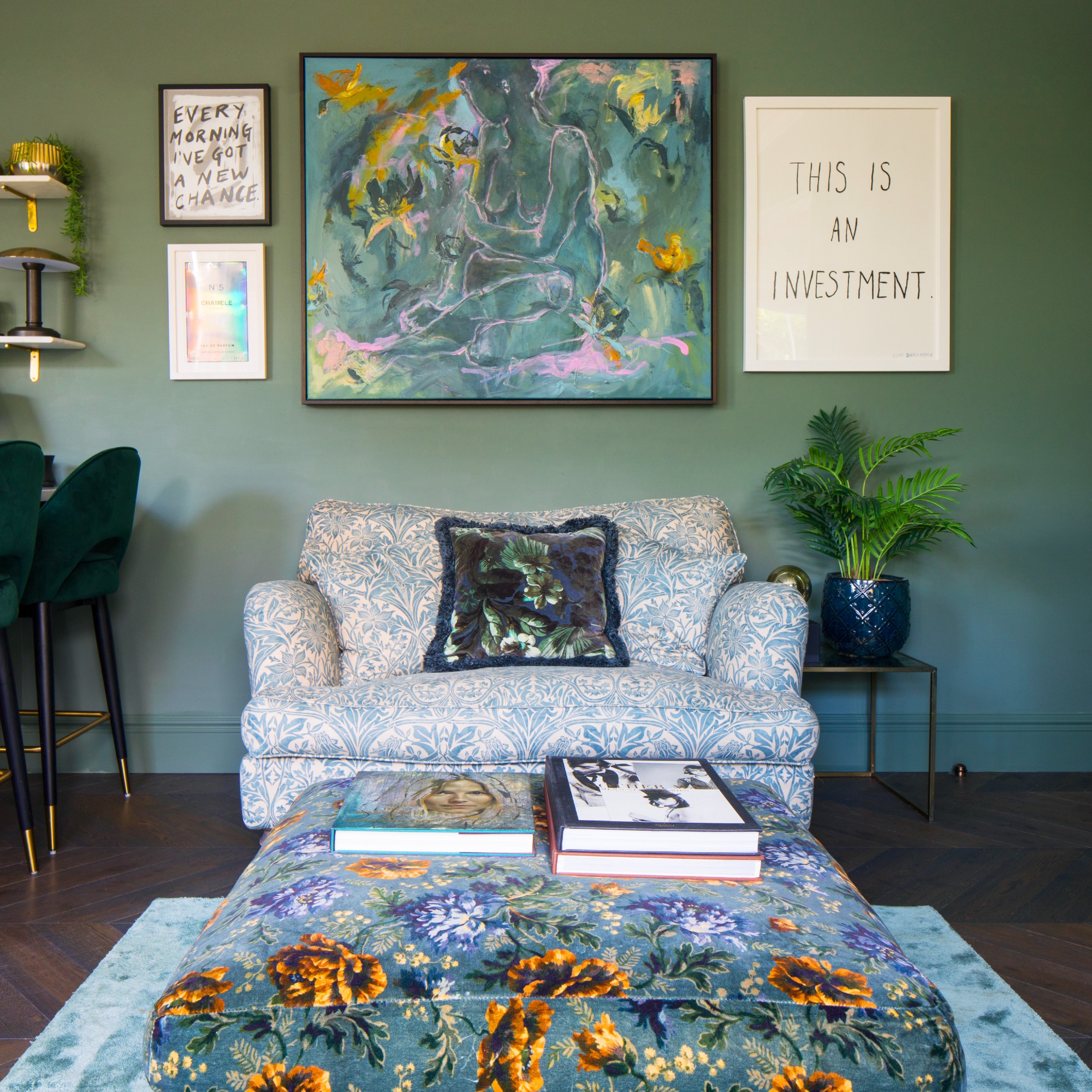 A green open-plan living room with a floral patterned loveseat and a floral ottoman in front of it used as a coffee table