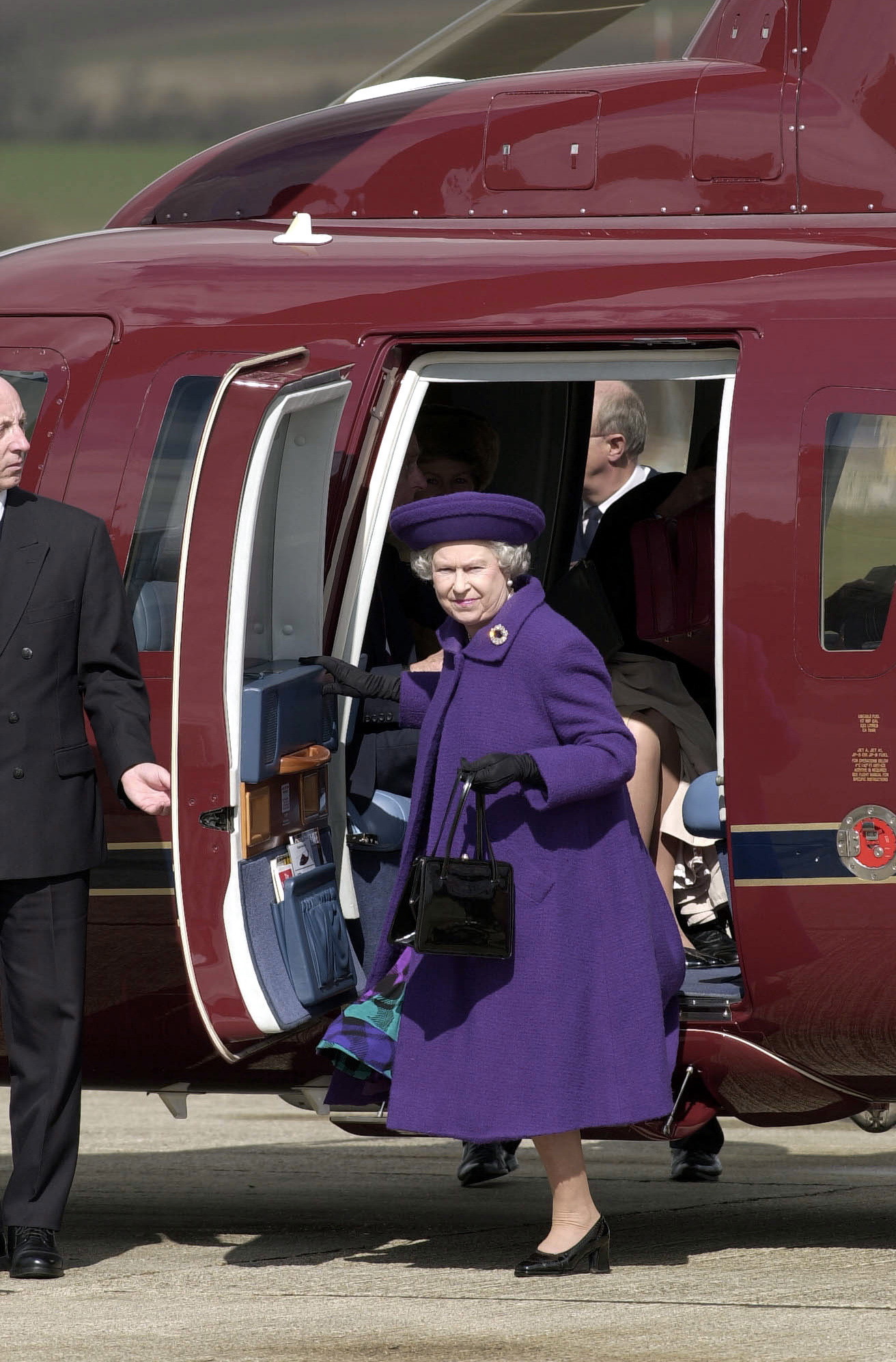 Queen Elizabeth wearing a purple coat stepping out of a helicopter