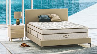Best mattress: the Saatva Classic luxury innerspring hybrid mattress placed on a faux leather bed frame overlooking a bright blue swimming pool