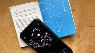 An iPhone with the app Sky View opened next to a book about star constellations