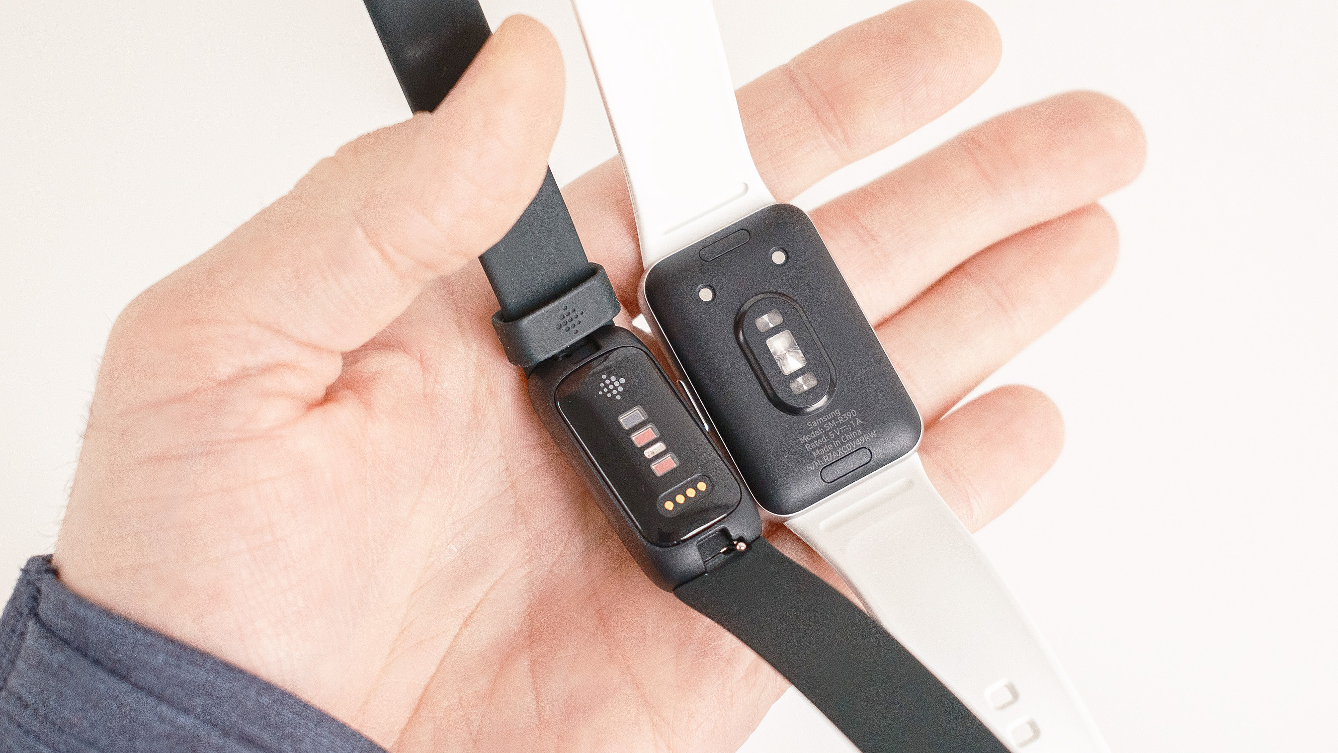 Close-up of the Samsung Galaxy Fit3 next to the Fitbit Inspire 3 in a user's hand