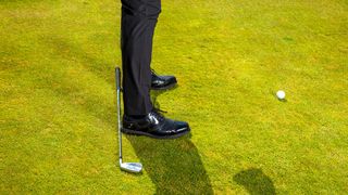 A club on the ground, behind the heels, to check the alignment in preparation of the golf swing