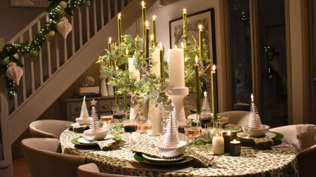 Pretty Christmas tablescape in compact open plan home with staircase in background. The table has a green and cream theme, with large church candles and ivy