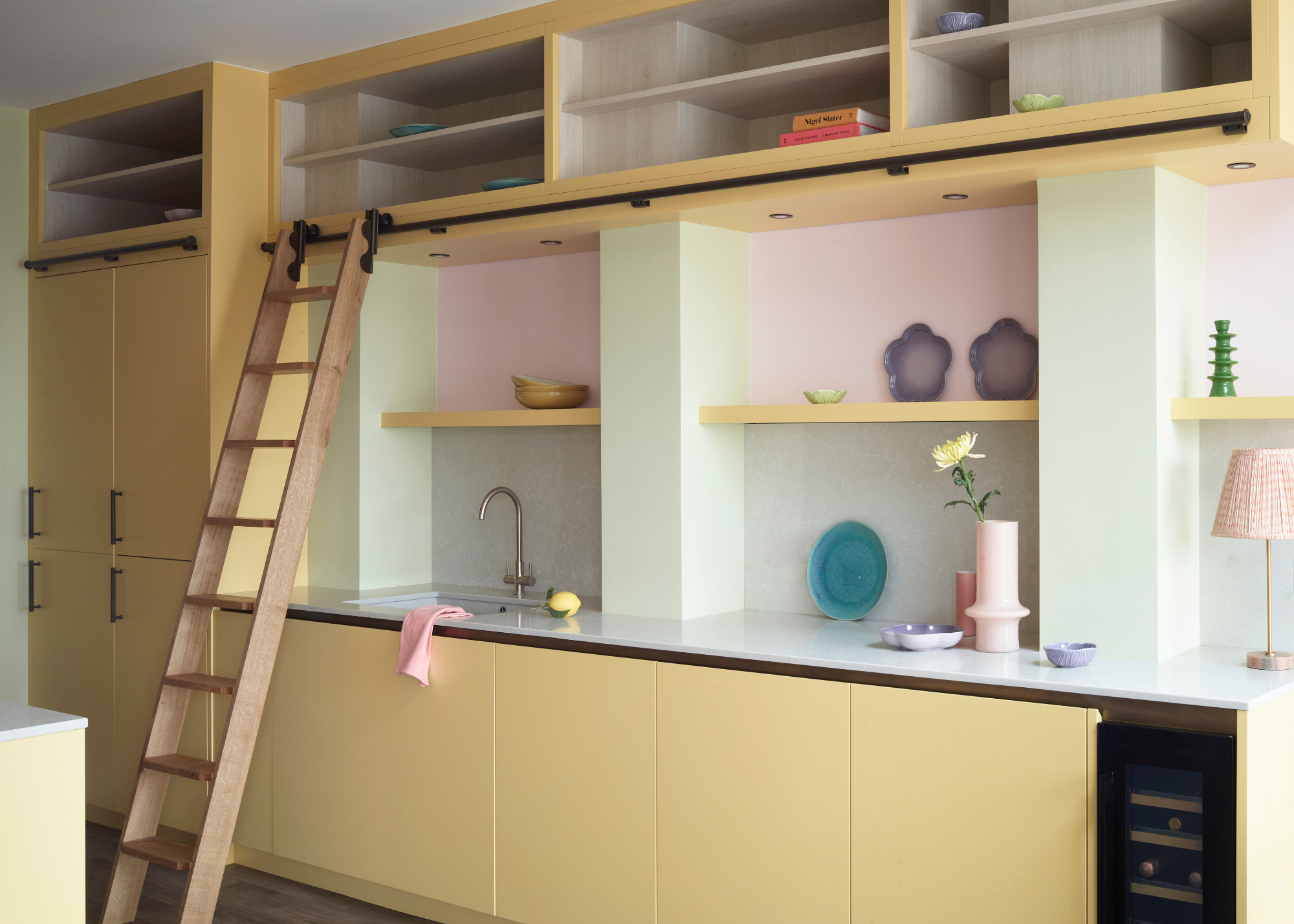 pastel-toned kitchen with yellow cabinets and pink walls. A sliding wooden ladder is connected to the wall