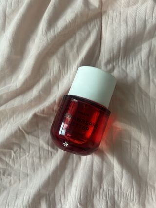 Bottle of Phlur Strawberry Letter perfume laying on light pink textured bed comforter