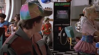 Michael J. Fox wearing a colorful hat and looking over his shoulder at a "Wild Gunman" video game.