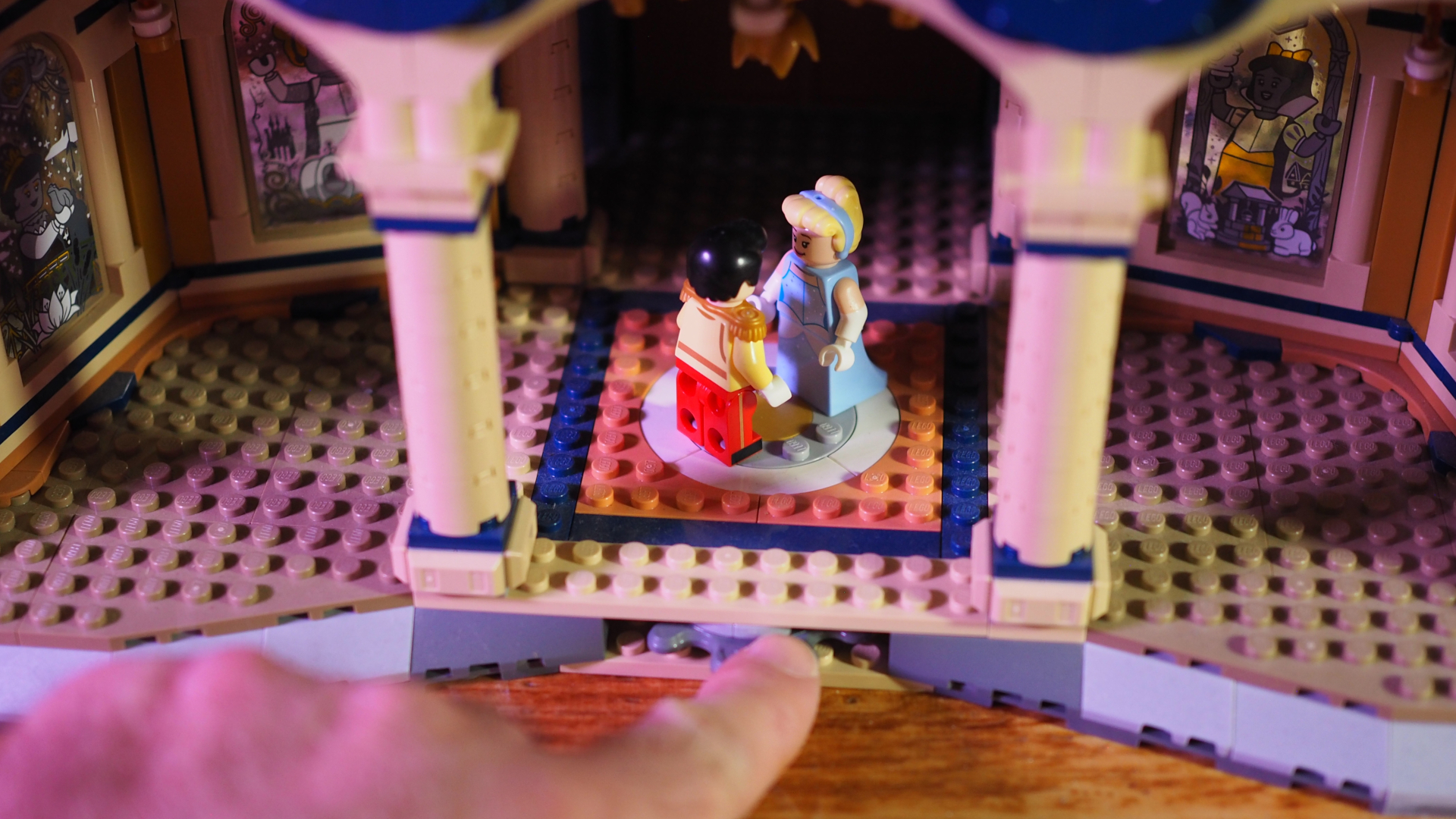 A hand moves a turnstile that makes minifigures of Cinderella and Prince Charming 'dance' in the Lego Disney Castle