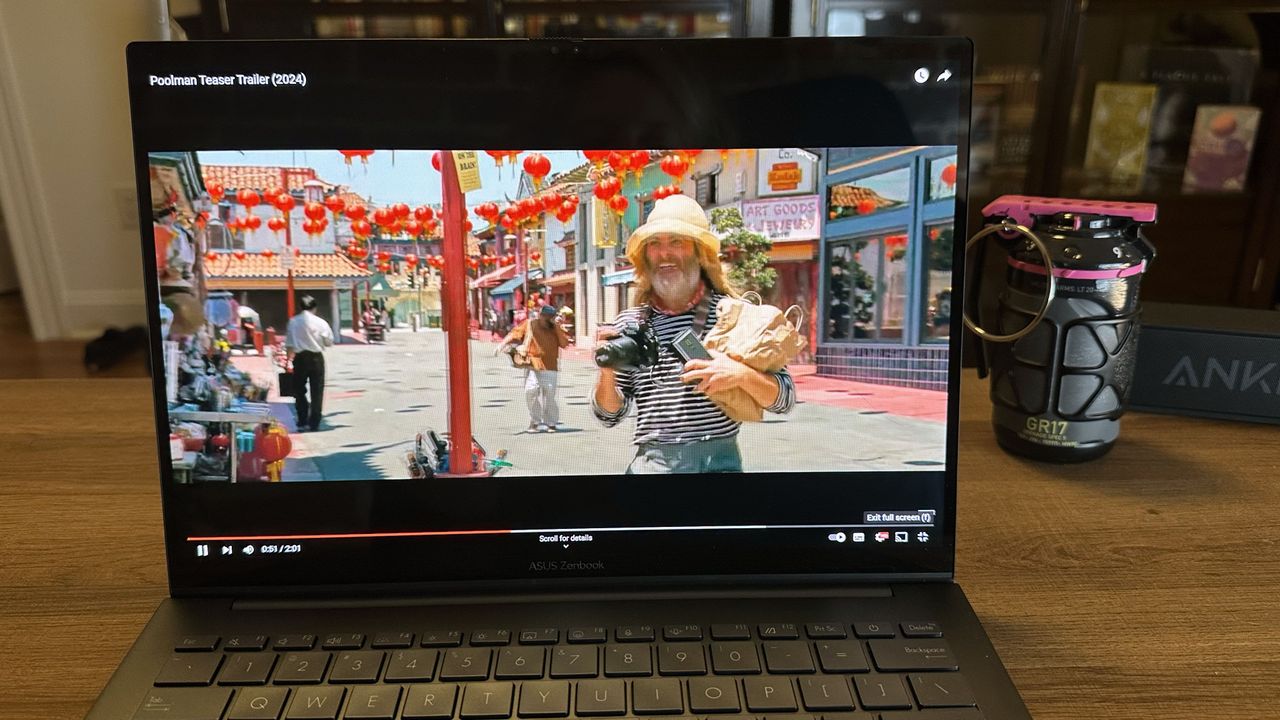 Asus Zenbook 14 OLED (Q425M) open on a wooden desk showing a movie trailer to demonstrate display brightness and vibrancy