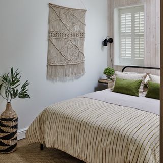 A bedroom with a macrame wall hanging, large rattan vase and striped bedding