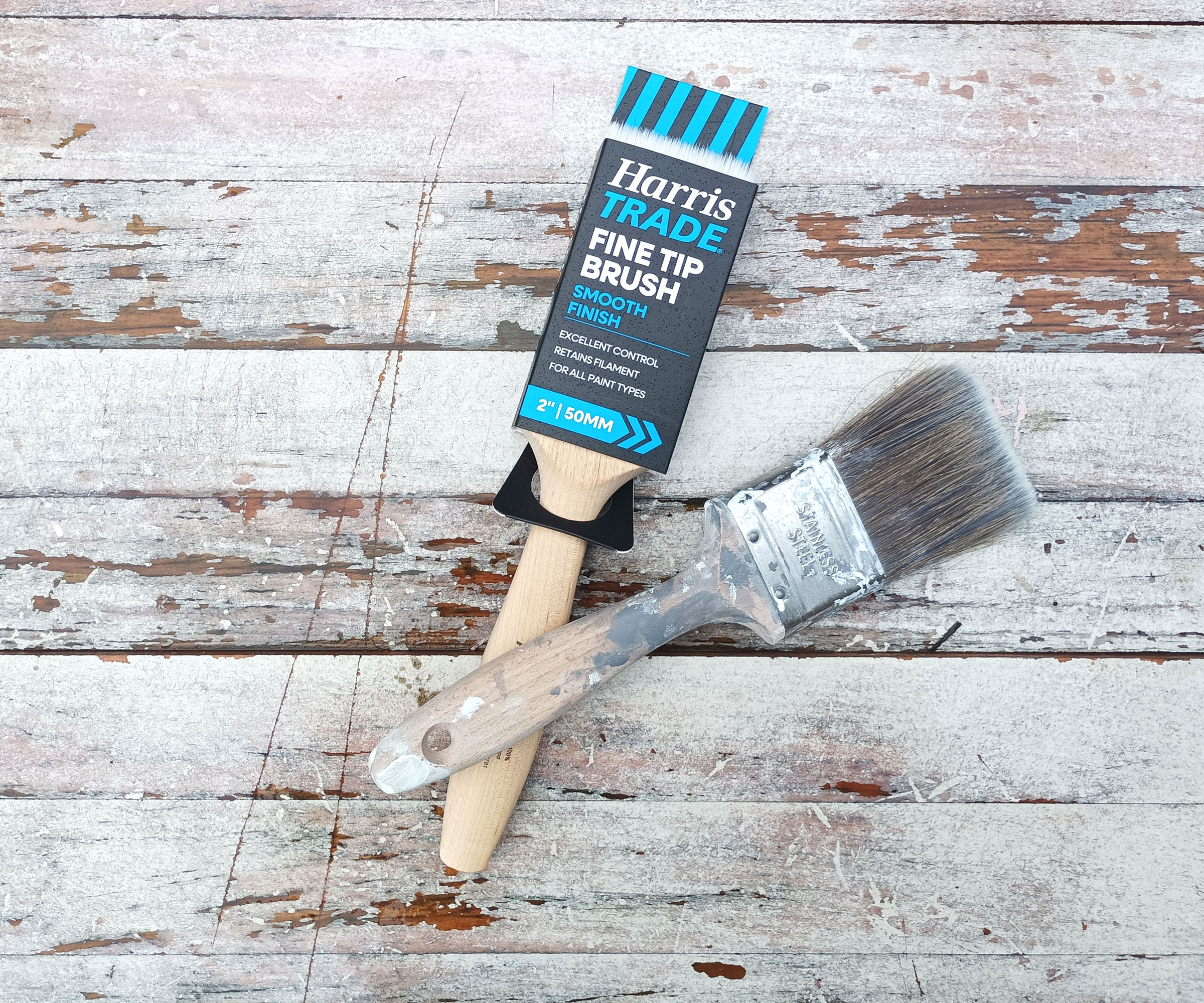 Two wooden two-inch paintbrushes - one in cover- on whitewashed wood background