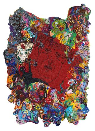 A fabric and beads tapestry features face and eye-inspired motifs in colorful, three-dimensional shapes, while its center reveals a face emerging from a red patch of textile.