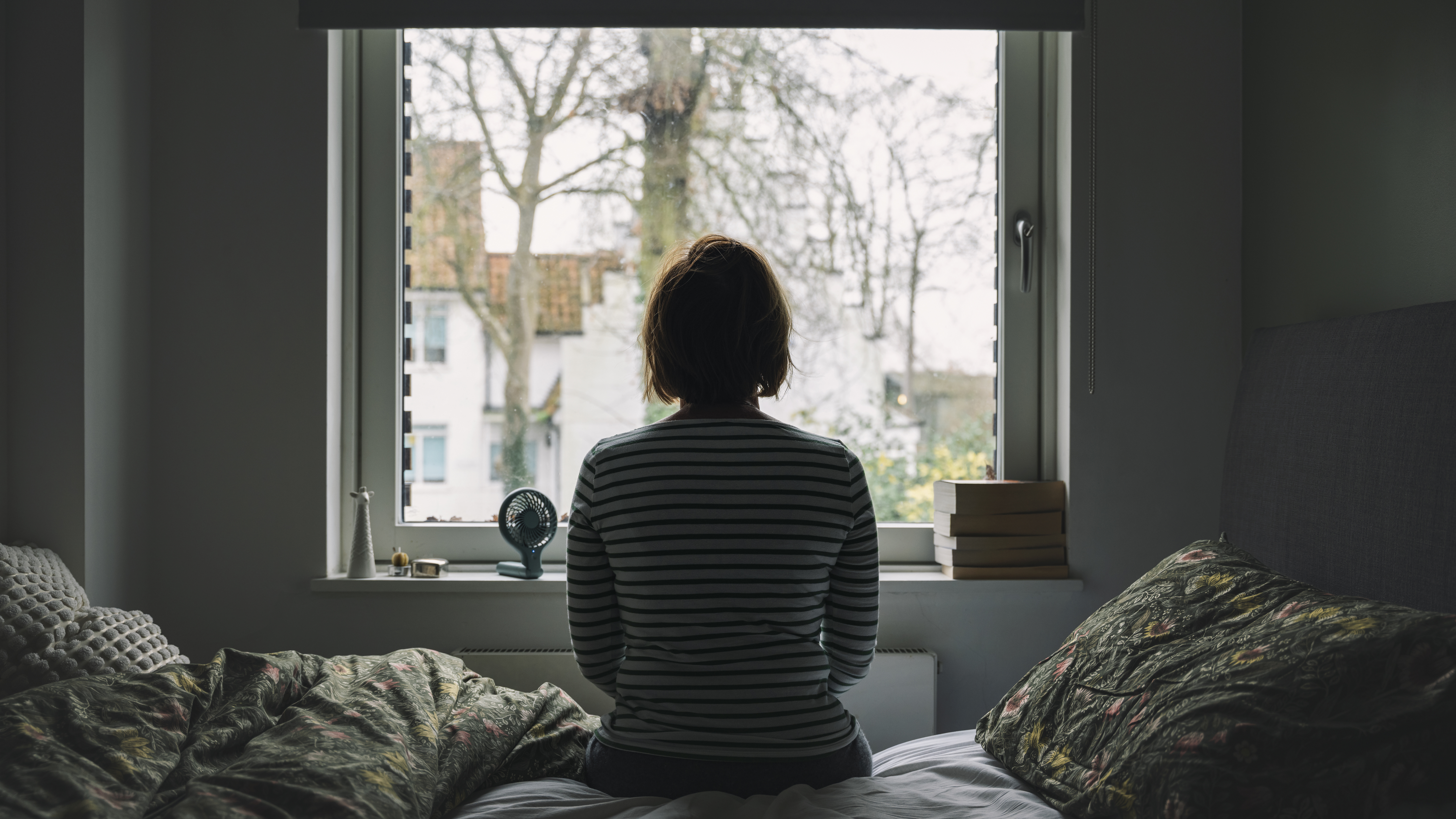 Rear view of a mature woman looking out of her bedroom window on a bright winter's day.